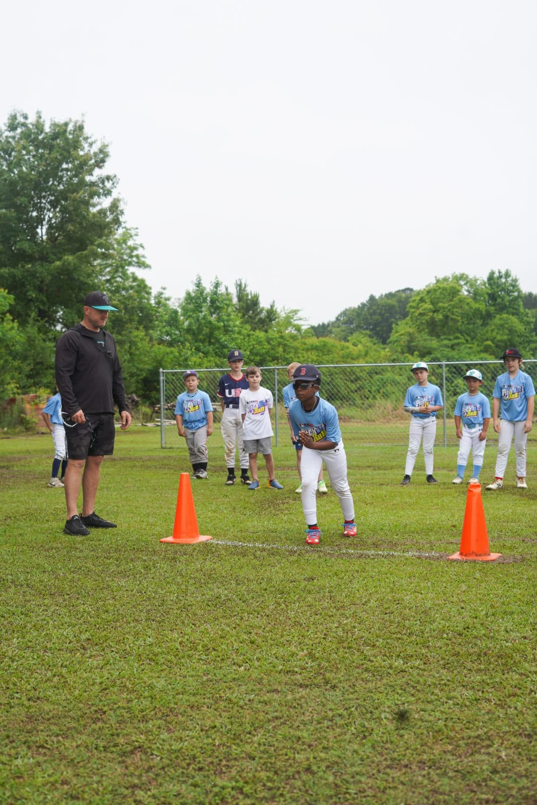 A camper in the ready position between cones for the running event as a coach looks on.