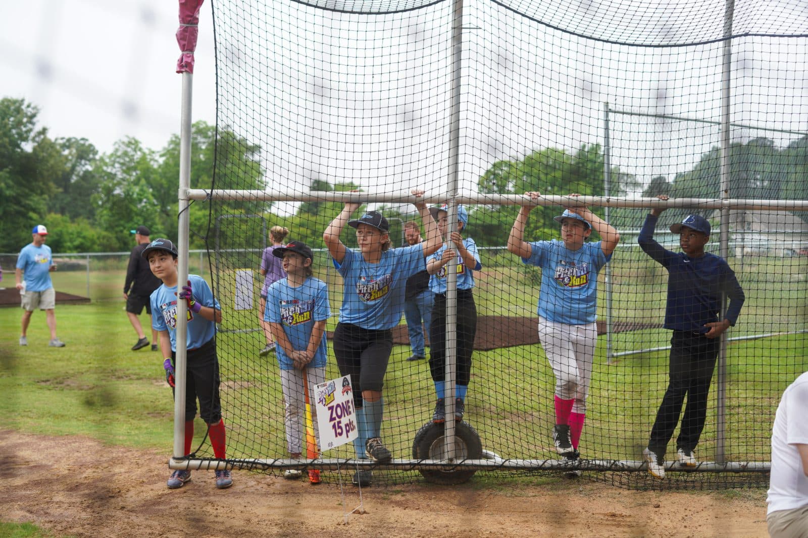 Players lined up along the fence beside the Zone 1 target sign.