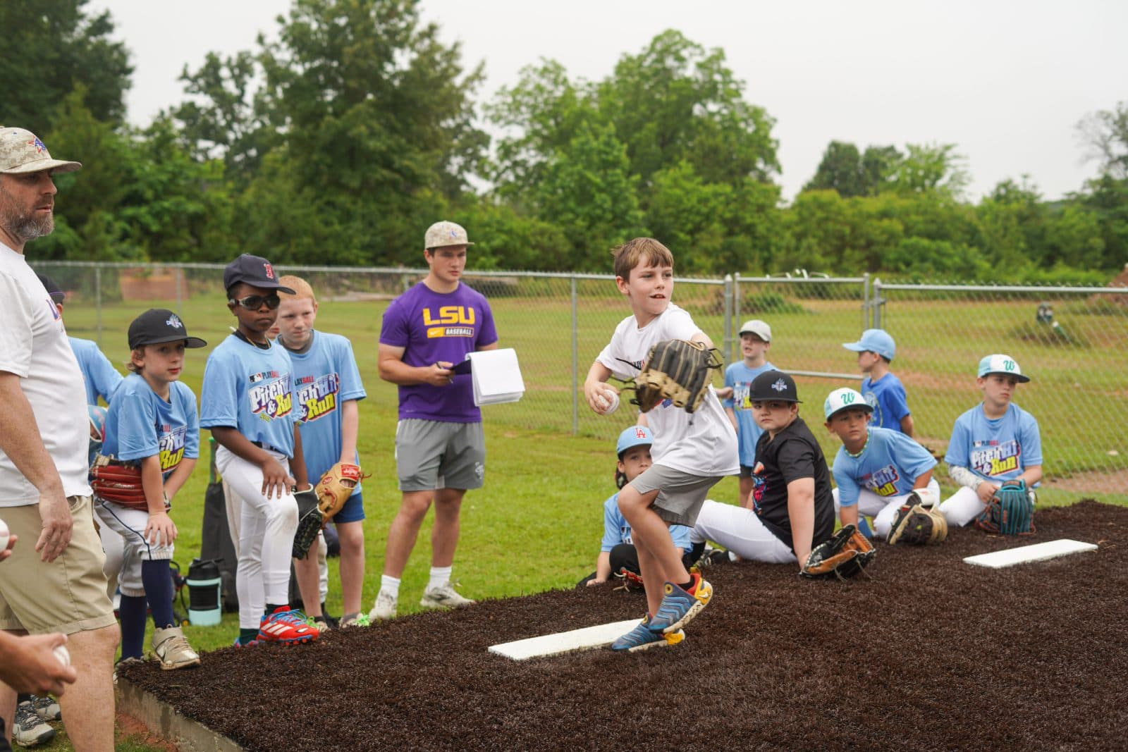 A young player pitching off the mound during MLB Pitch, Hit & Run as a coach and teammates watch.